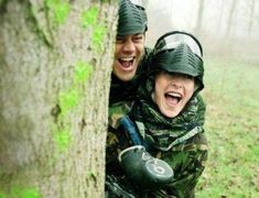 two people in camouflage jackets hugging each other behind a tree with their heads wrapped around them