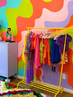 colorful clothing rack in front of wall with multicolored pattern on it and rug