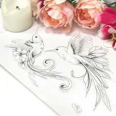 some flowers are sitting on a table next to a white candle and drawing paper with black ink