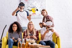 four people sitting on a yellow couch holding remotes and looking at the camera while one person holds a video game controller