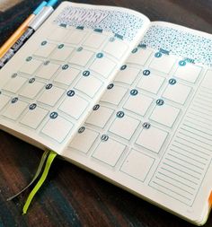 an open planner book sitting on top of a wooden table next to a pencil and marker