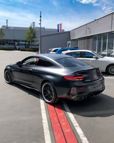 a black sports car parked in a parking lot next to other cars on the street