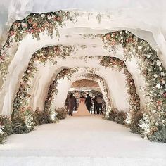 a group of people standing under an archway covered in flowers and greenery with white walls