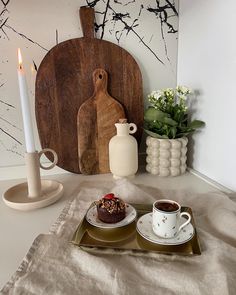 there is a plate with cake and coffee on it next to a vase, candle and cutting board