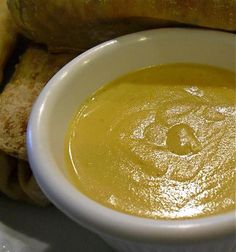 a white bowl filled with yellow liquid next to some bread pieces on a plate and in front of it