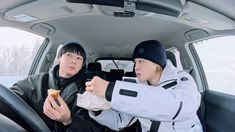 two young men sitting in the back seat of a car eating food and drinking soda