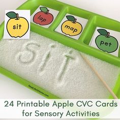 a green tray filled with lots of white sand next to two matching apples and letters