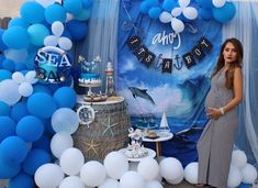 a woman standing in front of a table with blue and white balloons on it's sides