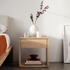 a white vase sitting on top of a wooden table next to a bed with an orange blanket