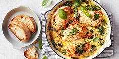 a skillet filled with chicken and spinach next to slices of bread on a table