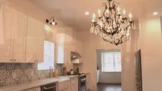 a chandelier hanging from the ceiling in a kitchen with white cabinets and counter tops