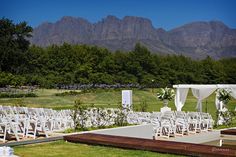 an outdoor wedding setup with white chairs and flowers on the lawn, surrounded by mountains