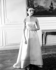 a woman in a white dress standing next to a table with a painting on it