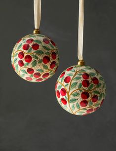 two ornaments hanging from strings on a gray background with red berries and leaves painted on them