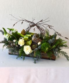 an arrangement of flowers and greenery in a wooden box on a tablecloth covered table