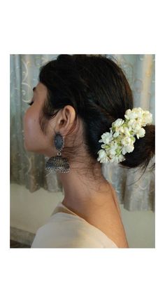 a woman with white flowers in her hair and earrings on top of her head, looking into the distance