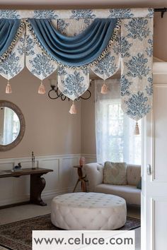 a living room filled with furniture and blue drapes hanging from the ceiling above a round ottoman