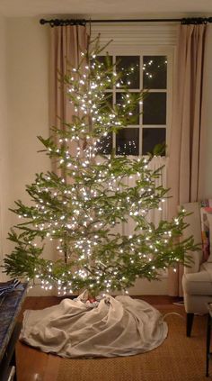 a white christmas tree with lights in a living room next to a couch and window