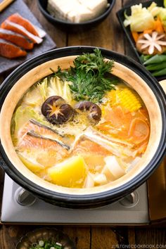 a bowl filled with soup and vegetables on top of a wooden table next to other dishes