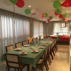 a long table with green and red balloons hanging from it's ceiling in a dining room