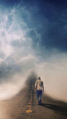 a man walking down the middle of a road under a cloudy blue sky with white clouds