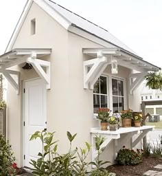 a small white house with potted plants on the porch