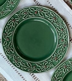 green plates with holly designs on them sitting on a doily next to napkins