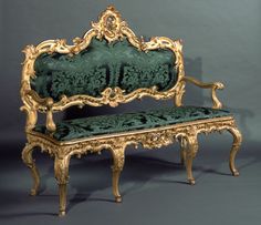 an ornate gold and green bench against a gray background with no one sitting on it