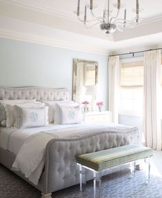 a large white bed sitting in a bedroom next to a chandelier and window