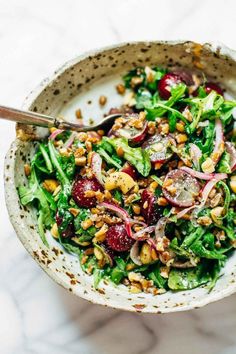 a white bowl filled with salad and topped with nuts