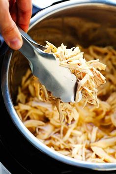 a person is spooning food out of an instant pot with the lid open and shredded chicken in it