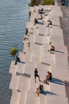 several people sitting on concrete steps near the water's edge, while one person is walking