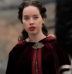 a close up of a person wearing a red dress and earrings with a man in the background