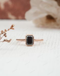 a black diamond ring sitting on top of a white table next to a flower arrangement