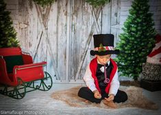 a young boy dressed in a top hat sitting on a rug next to a christmas tree