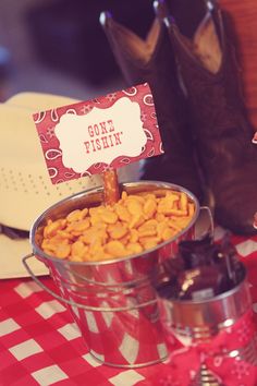 a red and white checkered table cloth with cowboy boots on it, one fishin'sign in a metal pail