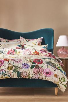 a bed with floral comforter and pillows on top of it in a room next to a lamp