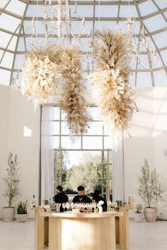 two chandeliers hanging from the ceiling above a table in a room with large windows