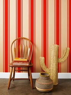 a chair next to a wall with red and white stripes on it, in front of a wooden cactus