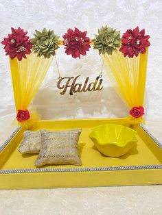 a yellow tray with red flowers on it next to a bowl and pillow in front of a sign that says haldi