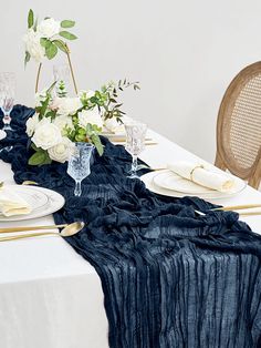 the table is set with white flowers and blue linens, gold place settings and silverware