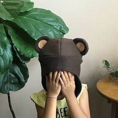 a person covering their face with a bear hat next to a potted plant on a table