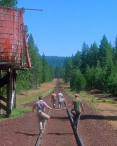 three men are walking on railroad tracks in the middle of an open field with trees