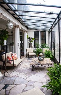 an enclosed patio with seating and potted plants in the center, surrounded by glass walls