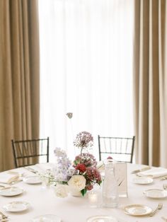 the table is set with white plates and silverware, flowers in vases, and candles