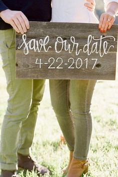 two people standing next to each other holding a wooden sign that says save our date