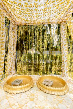 two golden trays sitting on top of a bed covered in yellow and white curtains