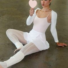 a woman sitting on the ground holding a heart shaped object in one hand and wearing white tights