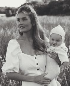 a woman holding a baby in a field