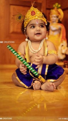 a baby sitting on the floor with a stick in his hand and wearing a headdress